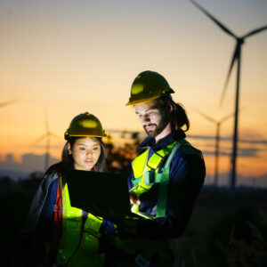 Multiracial colleagues examining wind turbines blueprints. Windmills on sunset